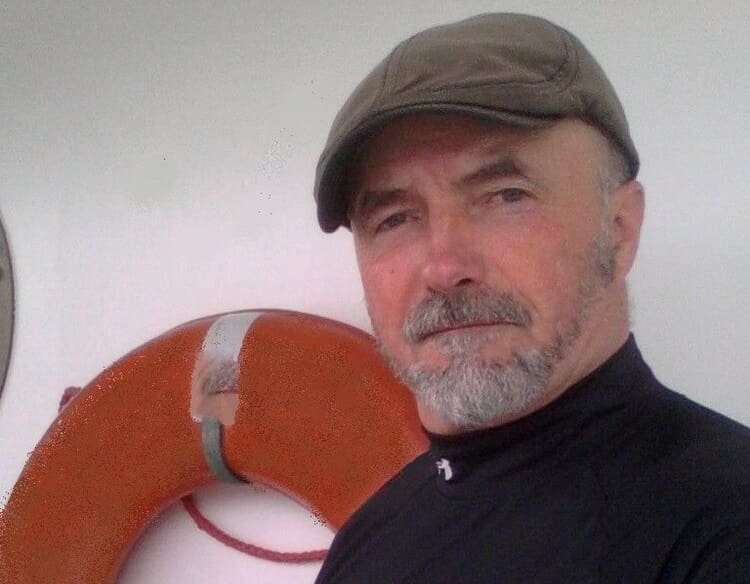 A man with a beard and hat standing in front of an orange life preserver.